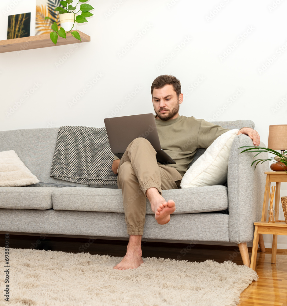 Man sitting on sofa at home and using laptop. Working from home. Home office.