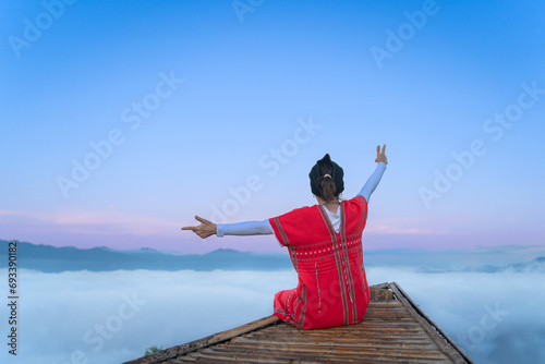 Asian traveler woman wearing Red Karen Dress is happy and relaxed with the sea mist of mountain peaks and beautiful natural scenery in the morning of Glor Selo Viewpoint at Mae Hong Son, Thailand.