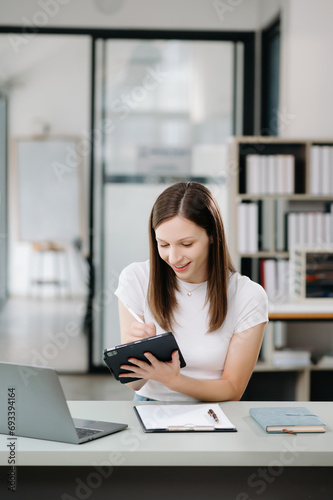 Confident woman with a smile standing holding notepad and tablet at the office.