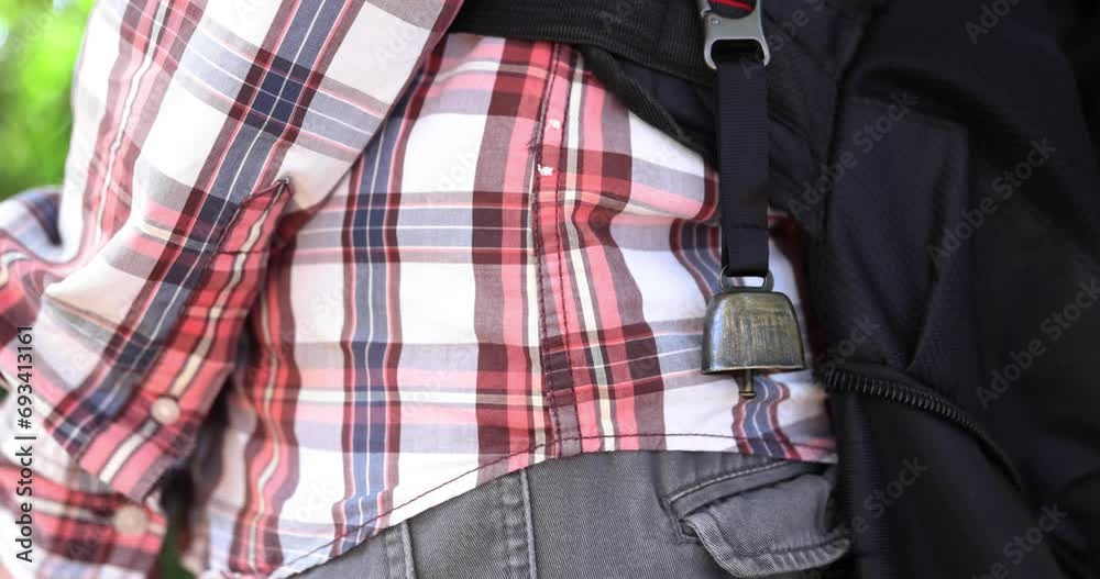 A person who wear a backpack with bear bell at the green forest in Autumn closeup