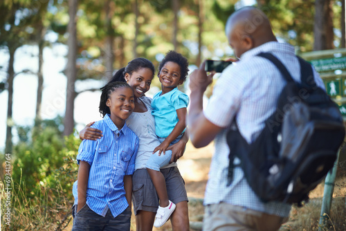 Smile, photograph and a black family hiking in the forest together for travel, tourism or adventure. Love, photography or memory with a man, woman and children in the woods or wilderness for freedom © Tasneem H/peopleimages.com