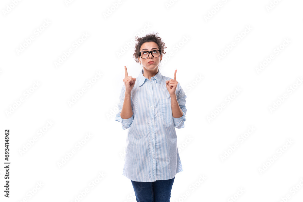 young fashionista caucasian woman with curly black hair in glasses is dressed in a blue blouse on a white background young fashionista caucasian woman with curly black hair in glasses is dressed in a blue blouse on a white background
