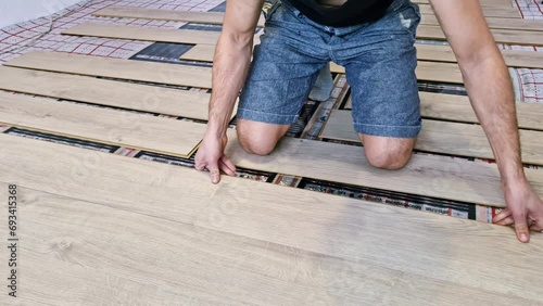 A young man working and using different tools. Close up of man installing underfloor heating and building wooden floor of a house.  photo