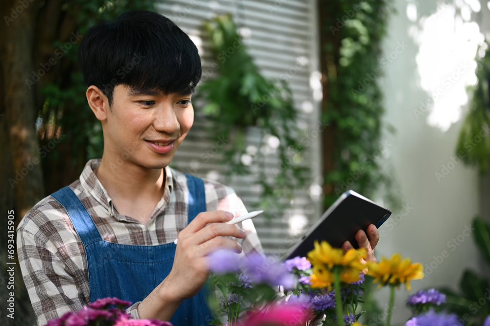 Portrait of happy Asian male florist in apron using digital tablet at small business flower shop. Portrait of happy Asian male florist in apron using digital tablet at small business flower shop.