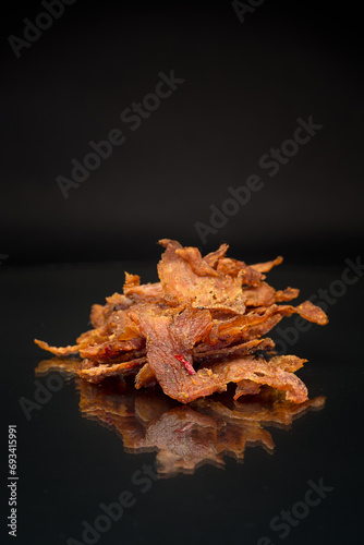 handful of dried meat marinated with spices, isolated on a black background.