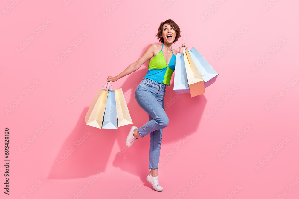 Full length photo of carefree fashionista young funny girl holding many shopping bags look empty space isolated on pink color background