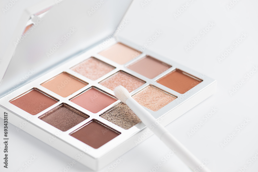 Eye shadow palette in nude beige shades with brush on a light background.