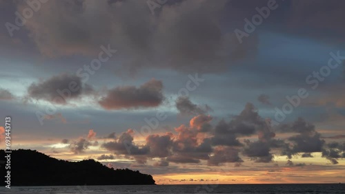 A bright tropical sunset over the ocean. The sun has disappeared. There are lilac clouds in the orange-lit sky. The waves roll towards the sandy beach, foaming. A hill in the distance. Malaysia.Borneo