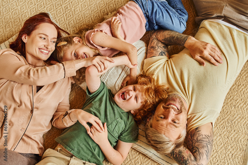 top view of happy parents and kids lying down and on floor and laughing in modern living room