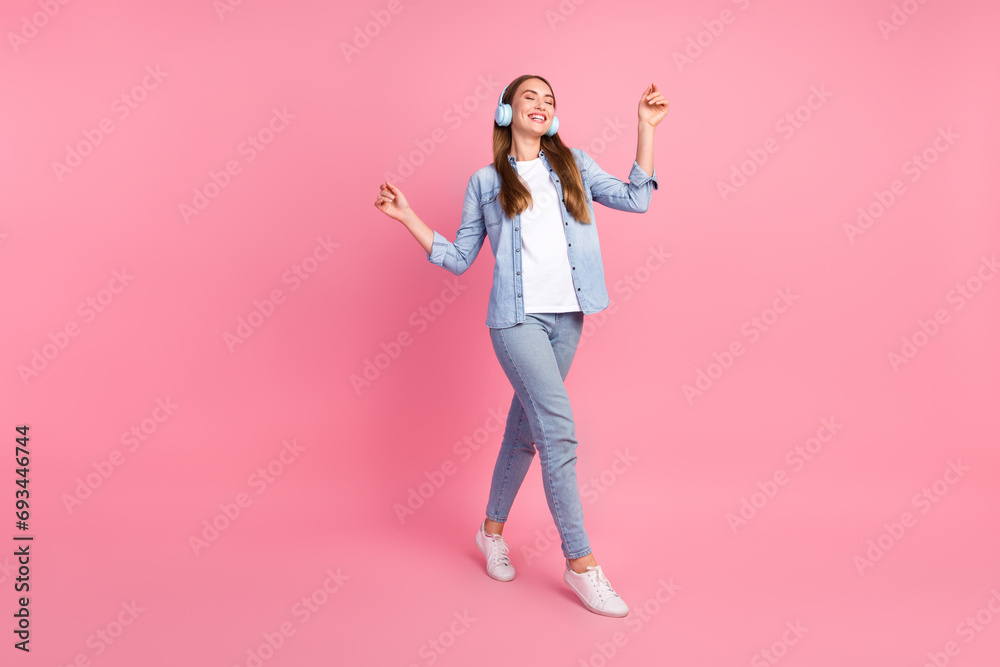 Full size photo of pretty young girl walking dance listen music earphones dressed stylish denim outfit isolated on pink color background Full size photo of pretty young girl walking dance listen music earphones dressed stylish denim outfit isolated on pink color background
