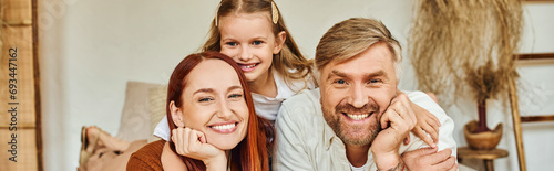 joyful parents with carefree daughter relaxing in bedroom and looking at camera, horizontal banner