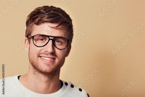 Portrait, smile and glasses with a man on space in studio for eyewear marketing on a tan background. Face, vision and a happy young geek or nerd on mockup for optometry advertising and information photo