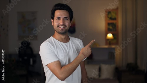 A man pointing fingers at the copy space at home - advertisement concept. A young smiling man pointing his index finger at something that stands out - a space for writing text photo
