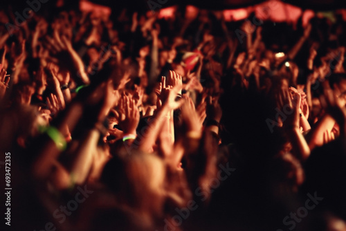 People, hands and crowd for music, festival and outside with arms raised for dancing, movement or enjoyment. Audience, concert and excitement with dj, band or singer with red, lighting and equipment