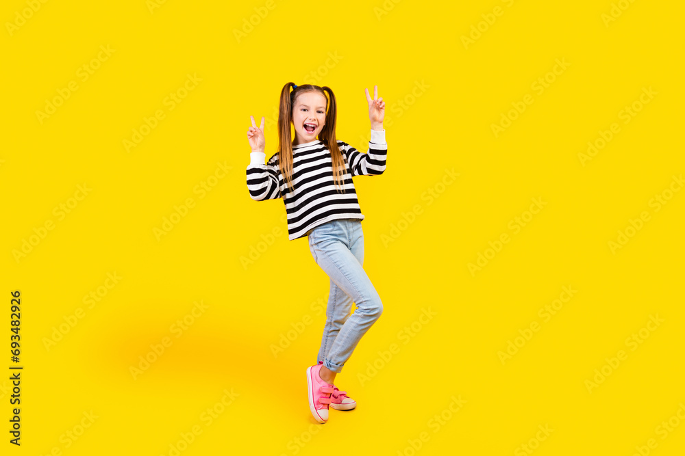 Full length photo of cheerful positive little child dressed striped pullover showing two v-signs isolated yellow color background