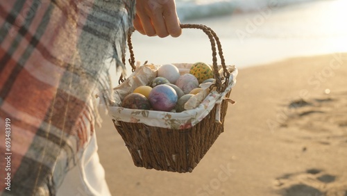 A young woman walks along the beach at sunset carrying a basket of Easter eggs. I'm walking towards the sun, the sea waves are behind me.