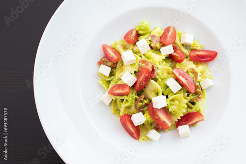 Bowtie pasta with cherry tomatoes, pesto, and feta cheese, and a large white bowl