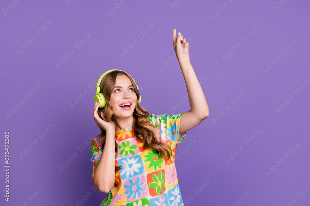 Photo of satisfied woman with wavy hair wear t-shirt touch headphones look directing up at empty space isolated on purple color background Photo of satisfied woman with wavy hair wear t-shirt touch headphones look directing up at empty space isolated on purple color background