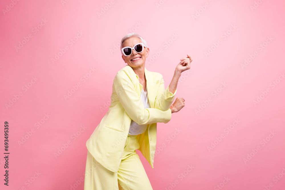 Photo of nice mature age positive lady wear yellow suit with stylish sunglasses dance rhythm relaxation isolated on pink color background - obrazy, fototapety, plakaty 
