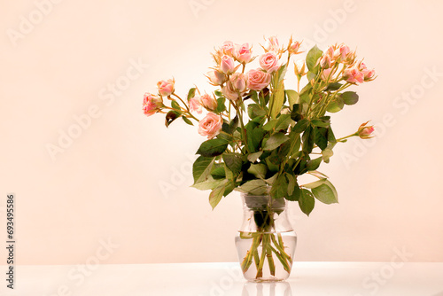 A bouquet in a transparent vase of apricot-colored bouquet roses, the trend color of apricot crash 2024, buds and open flowers . Greeting card element for 2024 fashion color project