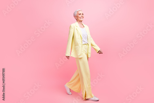 Full size photo of satisfied optimistic woman dressed yellow suit go to empty space look at sale isolated on pink color background