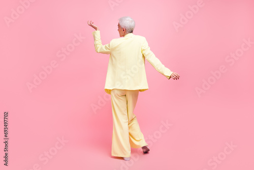 Full size photo of good mood elegant woman with white gray hair wear yellow suit turned with her back isolated on pink color background