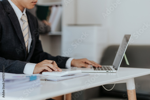 Asian male businessman working with laptop computer and smart phone with accounting documents at table in office Happy man working concept
