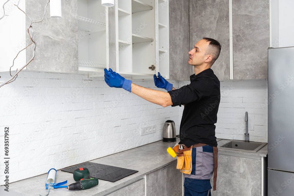 Worker installing door of cabinet with screwdriver in kitchen