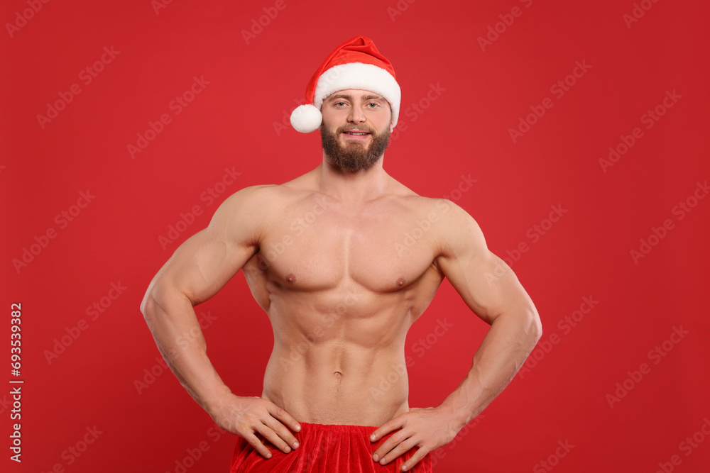 Muscular young man in Santa hat on red background