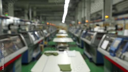 Blurred background view of working knitting machine in workshop. A row of industrial textil flat knitting machines in a knitwear factory. Manufacture of knitwear, modern computerized flat Knitting