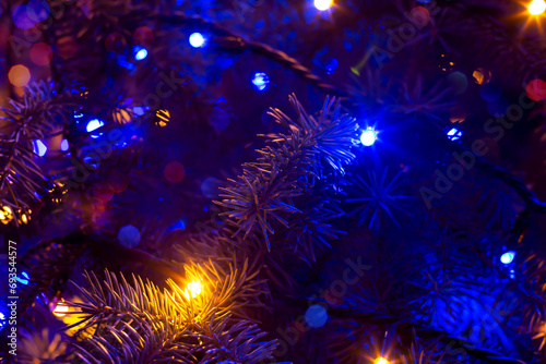 Christmas tree in dark illuminated with blue garland and blurred lights. Christmas and New Year background for design. Happy holidays. Selective focus, defocus