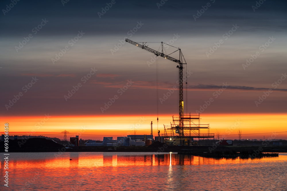 Fototapeta premium Construction of a new home with a crane during a very colorful dawn in Meerstad, Groningen.