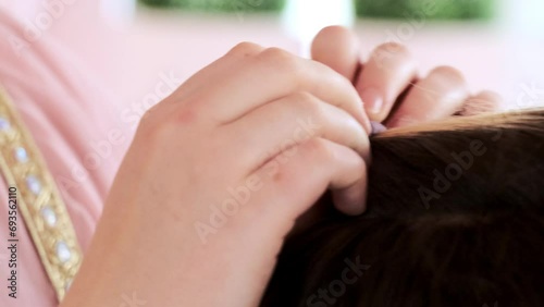 Young woman makes ponytail for brown haired female with blonde strand on blurred background. Person gathers hair with purple rubber band photo