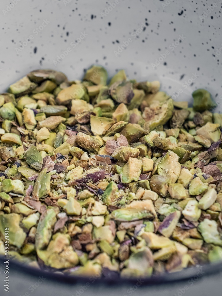 Powdered broken naked pistachio nuts in a white bowl on a wooden table Powdered broken naked pistachio nuts in a white bowl on a wooden table