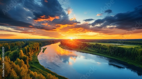 An aerial panoramic view of an idyllic rural sunset scene with a river and a dramatic colorful sky in the natural background.