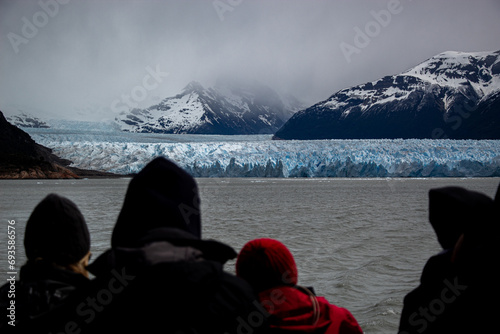 People watching from a distance the landscape offered by the Perito Moreno Glacier and the surrounding mountains from a boat on a cloudy day