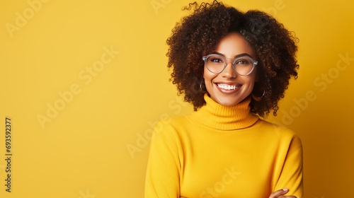A woman who is superstitious is holding her hands up for good luck, smiling positively, keeping her eyes closed, wearing spectacles, and casually hopping in a yellow background. this is a © Tahir