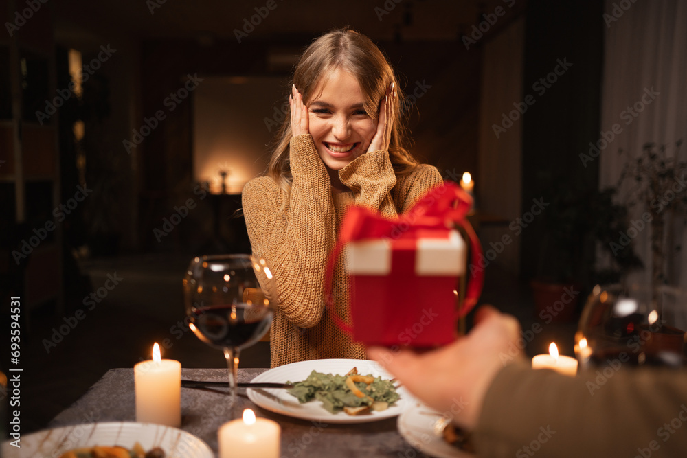 Beautiful loving couple is spending time together at home or restaurant. Man present gift box his wife and having romantic dinner. Celebrating saint valentine's day concept.