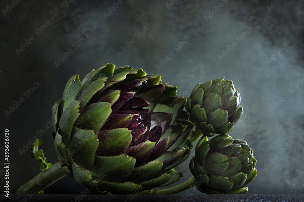 Obraz premium Fresh green artichoke on a blurred background. Artichokes on a dark background. Copy space.
