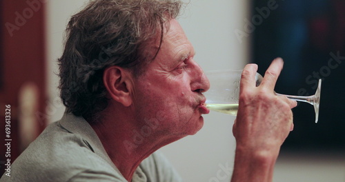 Senior man drinking wine at home casually. Casual candid older retired man drinks glass white wine © Marco