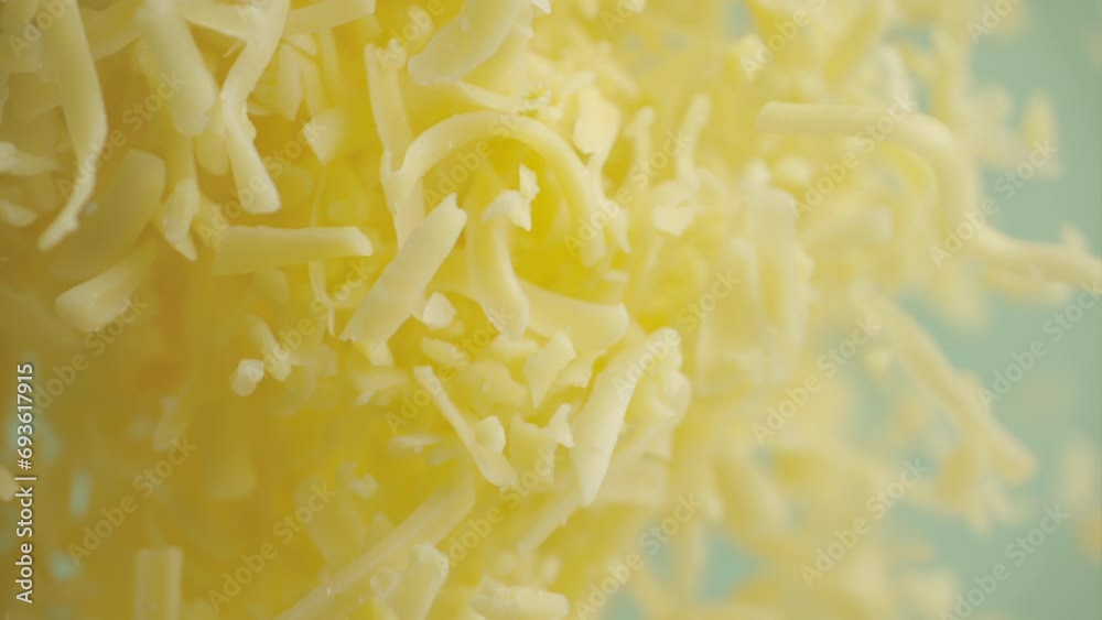 Heap grated cheddar cheese flying in slow motion close up. Shredded yellow parmesan cheese falling in macro Heap grated cheddar cheese flying in slow motion close up. Shredded yellow parmesan cheese falling in macro