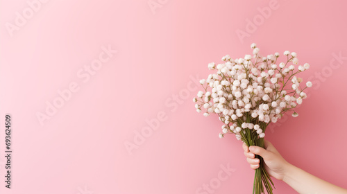 A hand with a delicate arrangement of baby's breath, bouquet of flowers, plain background, with copy space