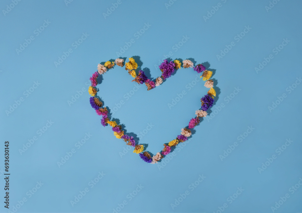 heart made of flowers on a blue background. flowers of different colors yellow pink white and purple