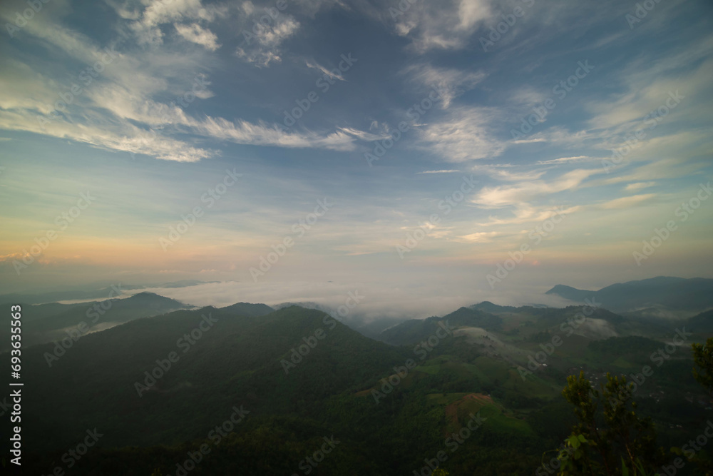 Obraz premium The stunning view from a tourist's standpoint as they go down a hill on a foggy trail with a hill and a background of a golden sky in Forest Park, Thailand. Bird's eye view. Aerial view.