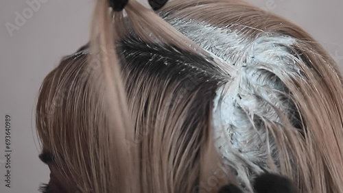 blonde paints over the dark hair roots on her head with hair dye, closeup