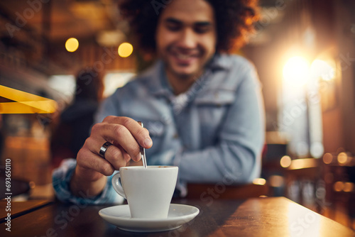 Young man sitting in cafe stirring or mixing a coffee mug photo