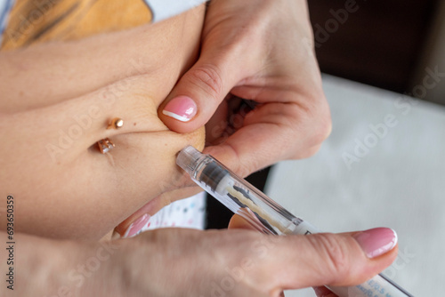 Close up shot of the woman with beautiful hands  preparing hormone medicine and injecting herself to the abdomen with pierced bellybutton. Healthcare