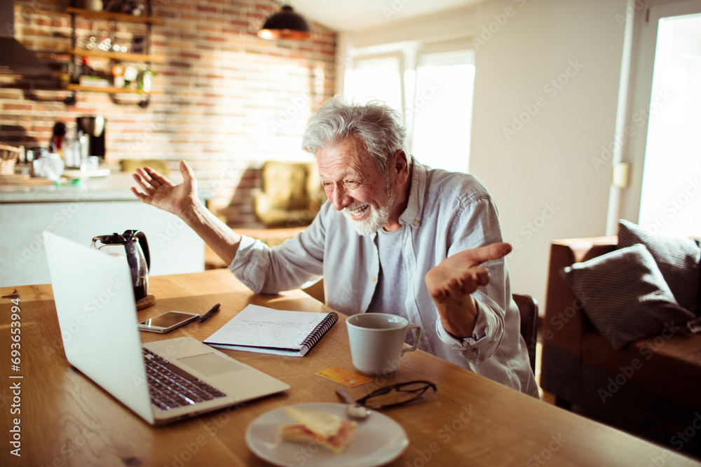 Senior man working at home with laptop and papers on desk Senior man working at home with laptop and papers on desk