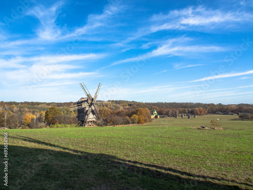Old wooden windmill in field with green grass and blue sky, sunny day.