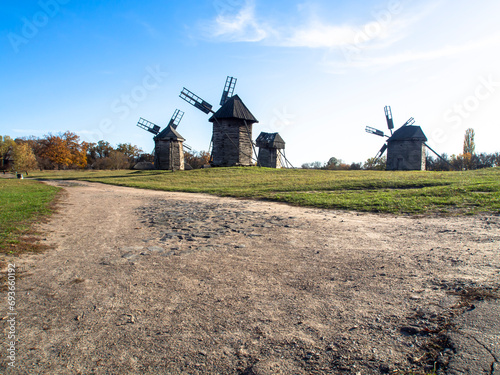 Group of old wooden windmills in field with green grass and blue sky, sunny day.